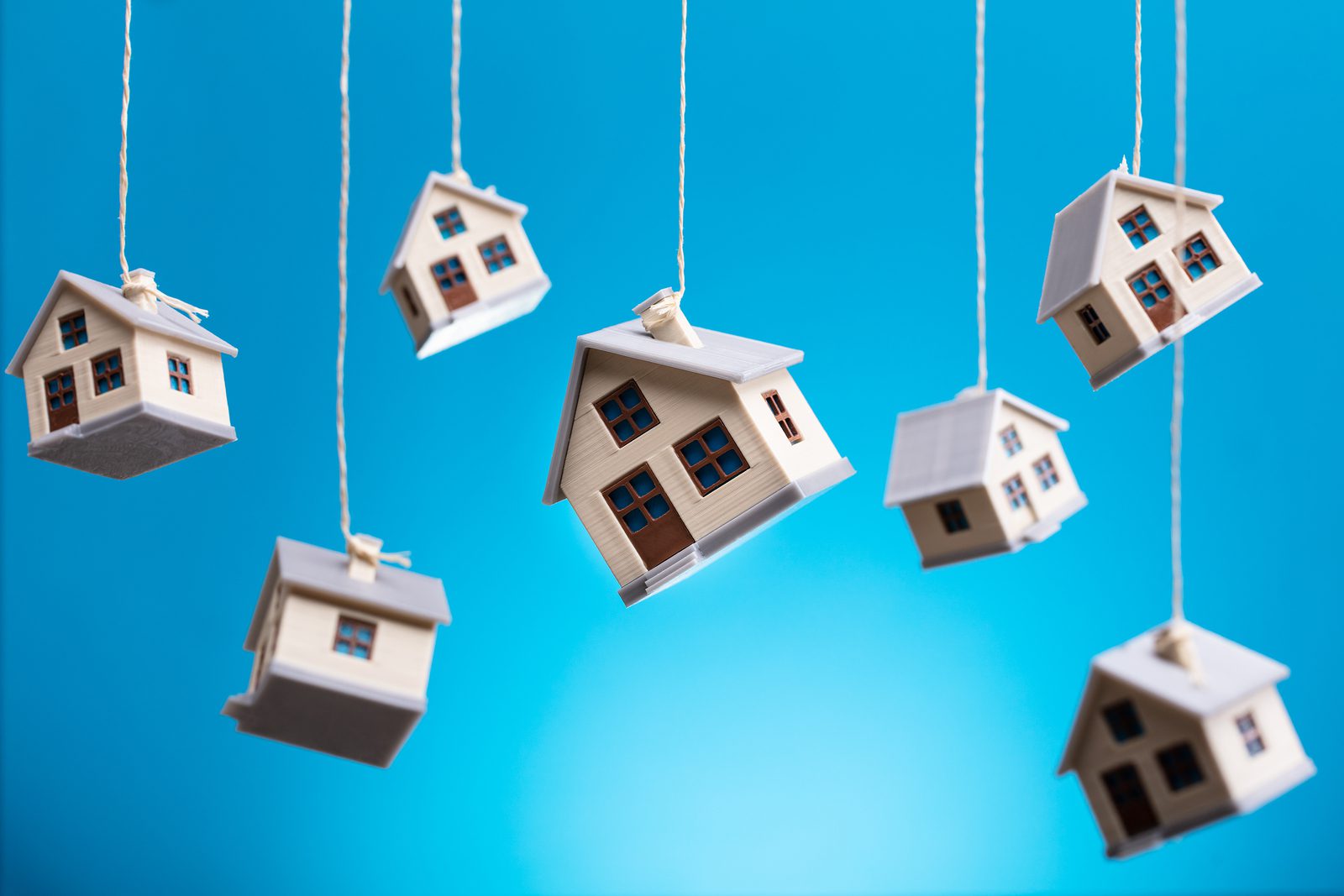 Miniature Houses Hanging By Strings Against Blue Background